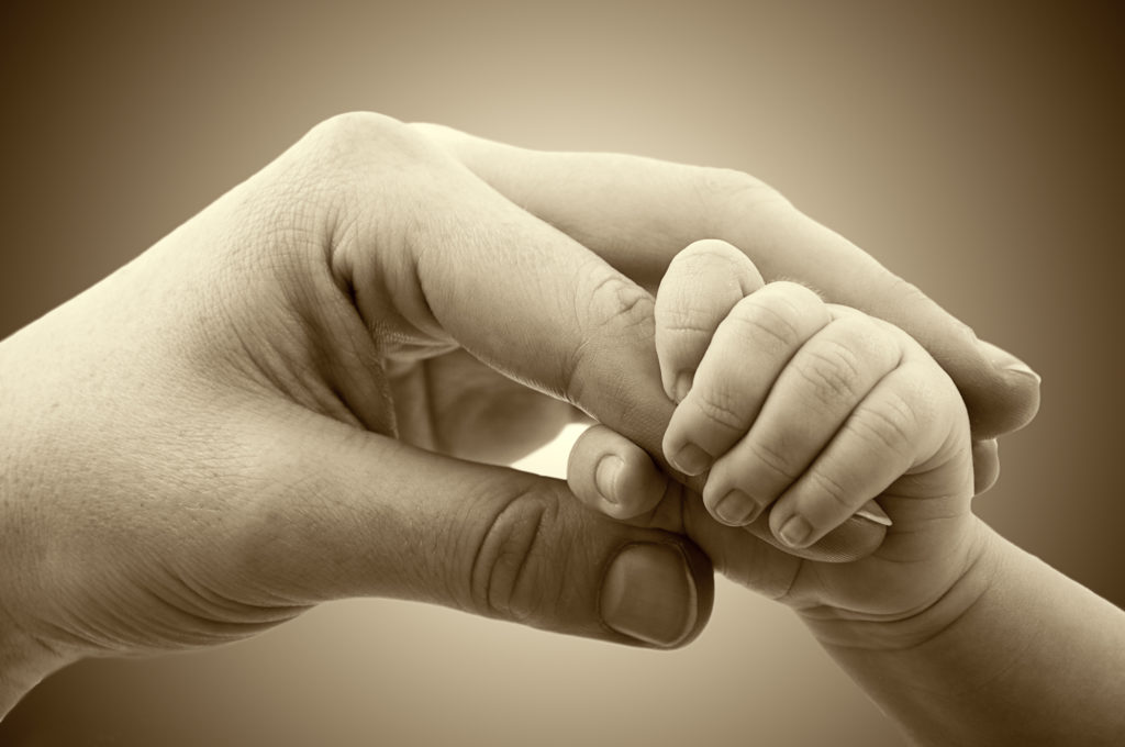 Image of mother's hand intertwined with infant hand as we learn about the importance of revocable trust 